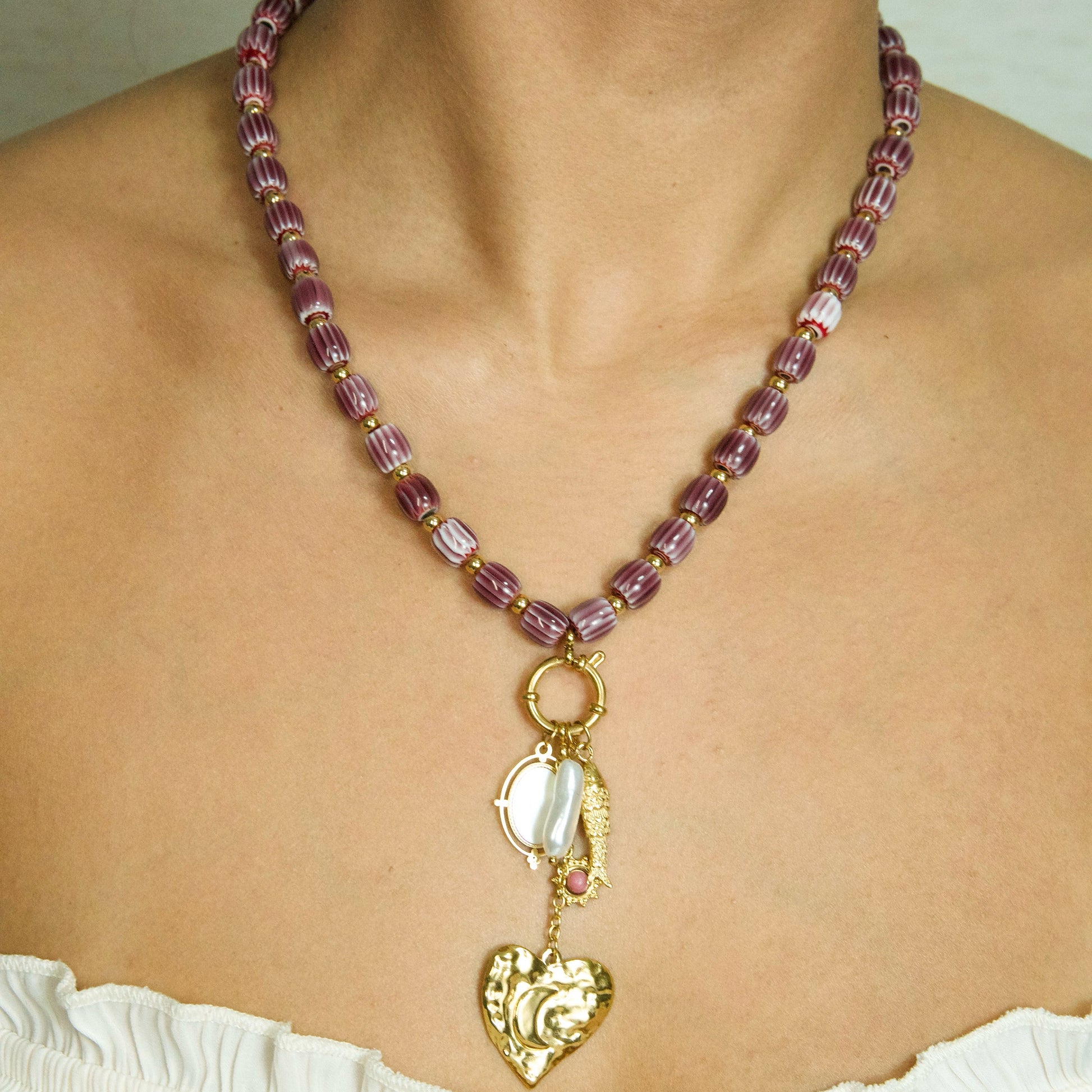 Necklace with purple beads and gold heart pendant on a person wearing a white top.