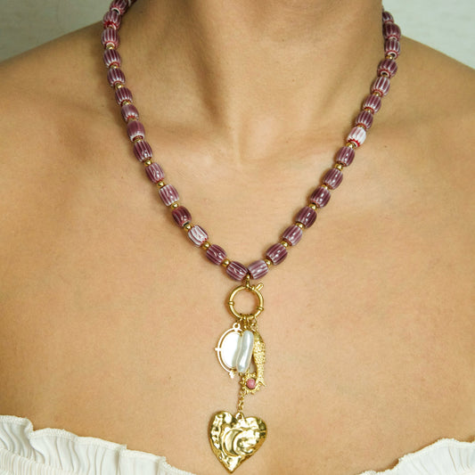 Necklace with purple beads and gold heart pendant on a person wearing a white top.