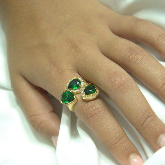 Hand wearing a gold ring with green gemstones on a white background
