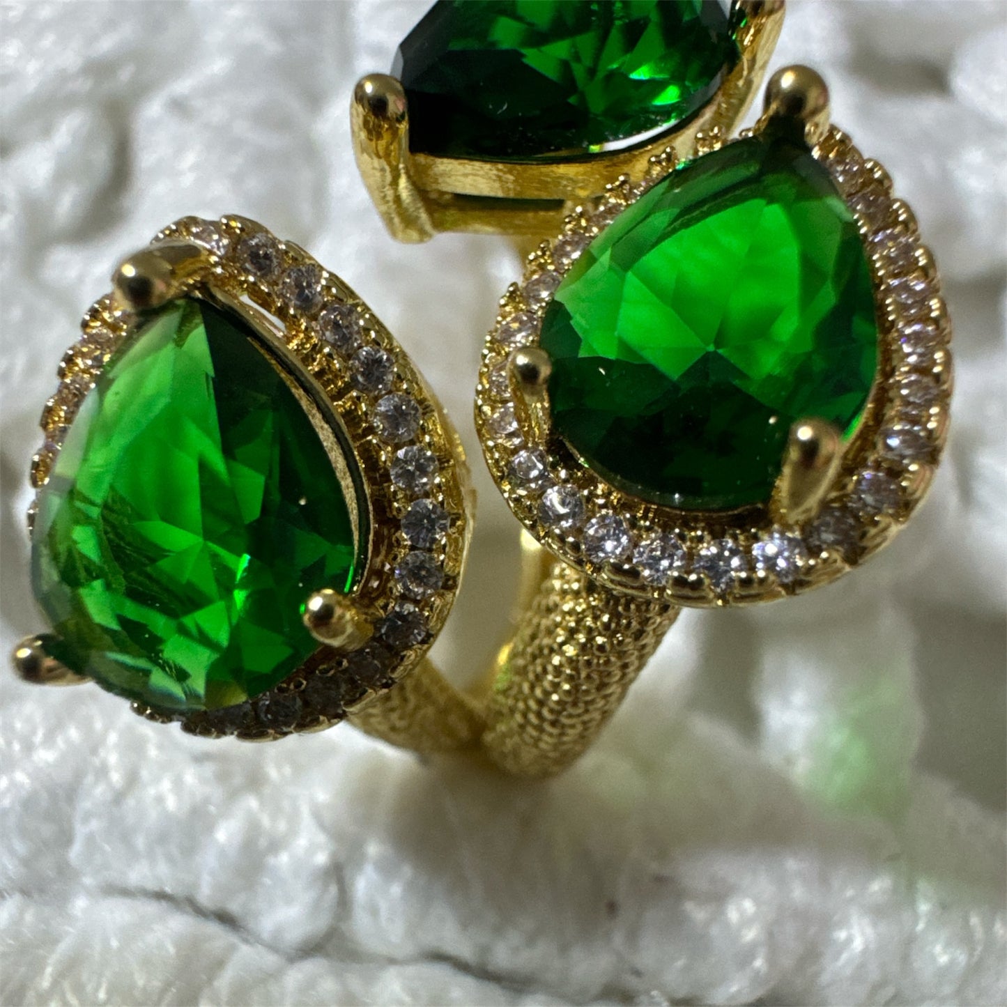 Gold ring with green gemstones on a textured white background