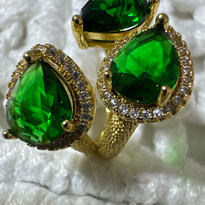 Gold ring with green gemstones on a textured white background